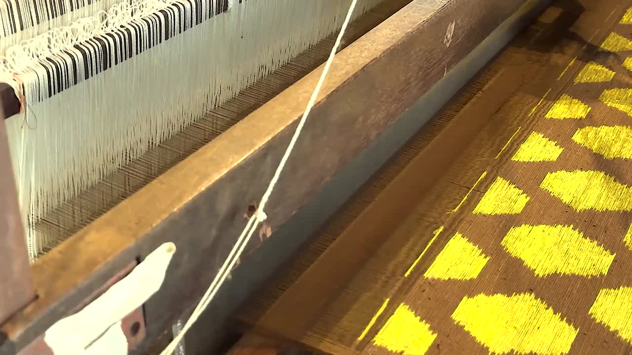 Detailed view of yellow geometric patterns being woven on a traditional loom.