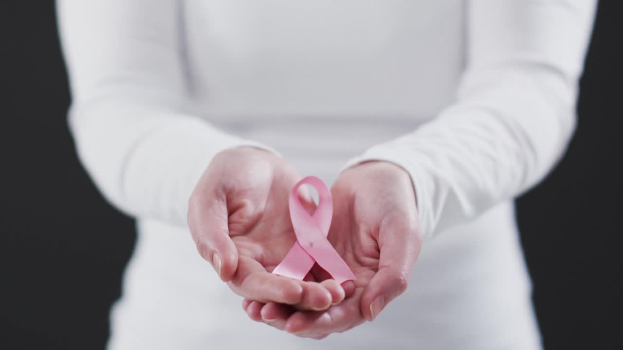 Parte centrale del corpo di una donna che tiene un fiocco rosa su sfondo nero