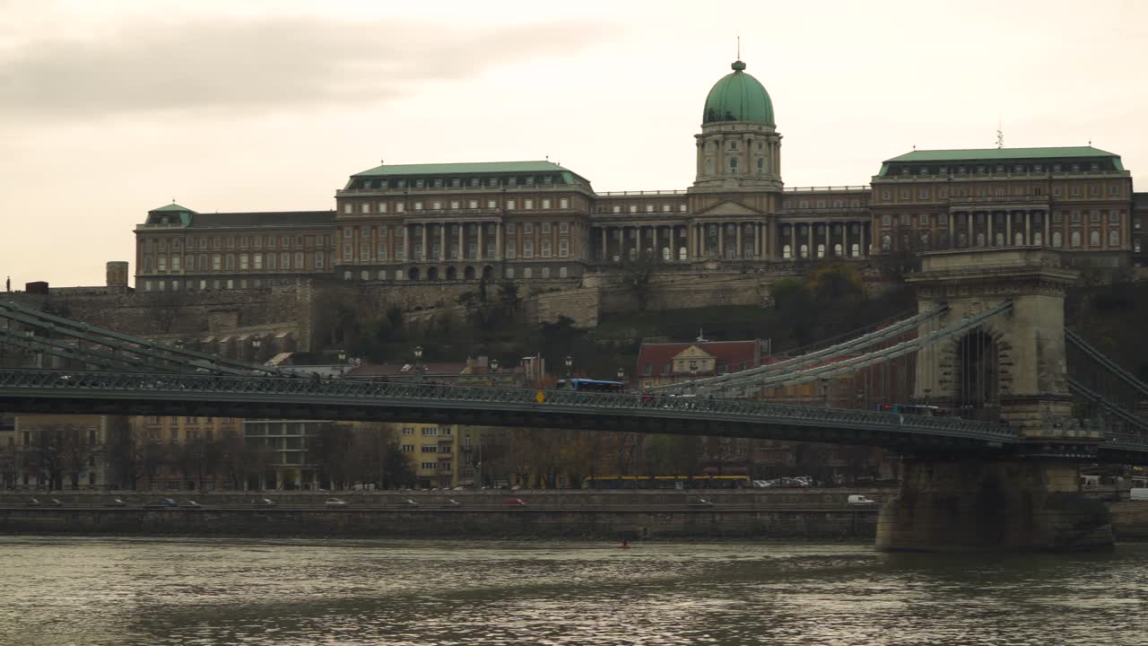Transport Vehicles Driving On The Szechenyi Chain Bridge In Budapest Hungary - A Beautiful Wrought Iron And Stone Bridge Spanning The Danube River With Buda Castle In The Background - Panoramic Shot