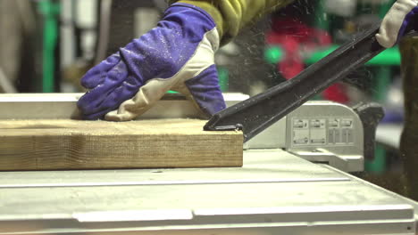 craftsman using metal rod to push wooden plank into saw for protection