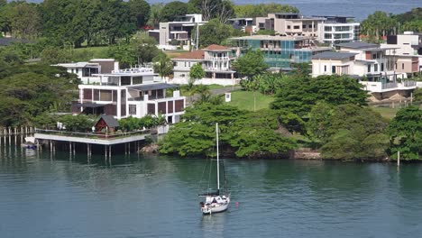 sailboat floating in the sea with luxury waterfront villas in kota kinabalu, sabah, malaysia. - wide shot