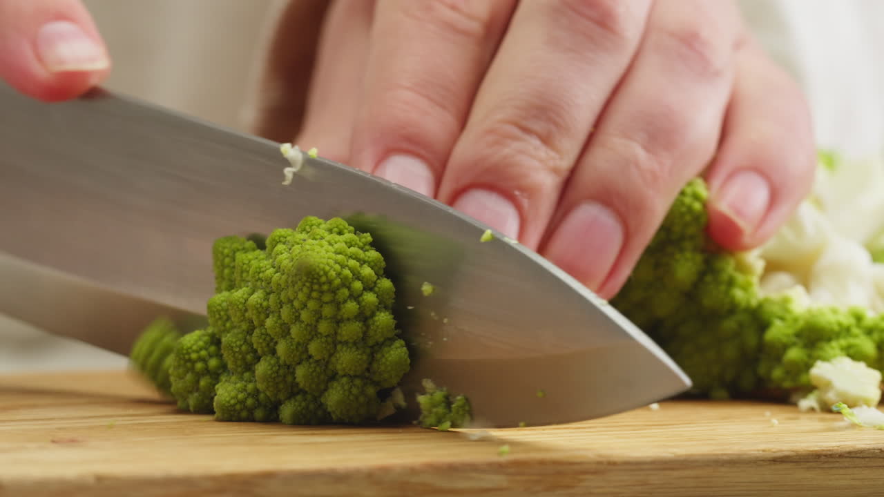 Close-up of Hand Cutting Fresh Romanesco Broccoli on a Wooden Board