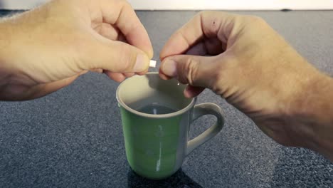 person opening pill capsule and pouring white powder into a cup mug