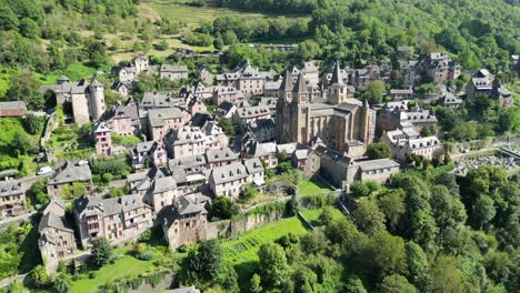 drone aerial view in france countryside small old medieval town and a cathedral surrounded by a green mountain forest circling around in conques