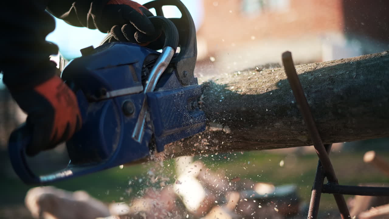 Man in gloves is choping wood using a chainsaw. Close view