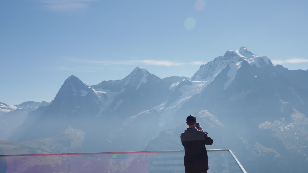 usando su teléfono inteligente, un turista está documentando la impresionante variedad de montañas cubiertas de nieve desde una torre