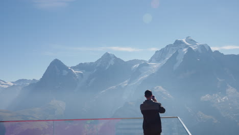 using their smartphone, a tourist is documenting the breathtaking range of snow-covered mountains from a tower