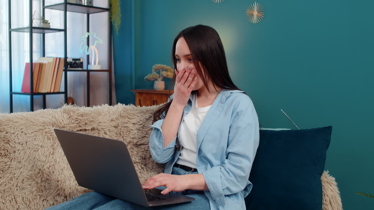 Woman emotionally celebrating success at laptop covering mouth surprised waving hands disbelief