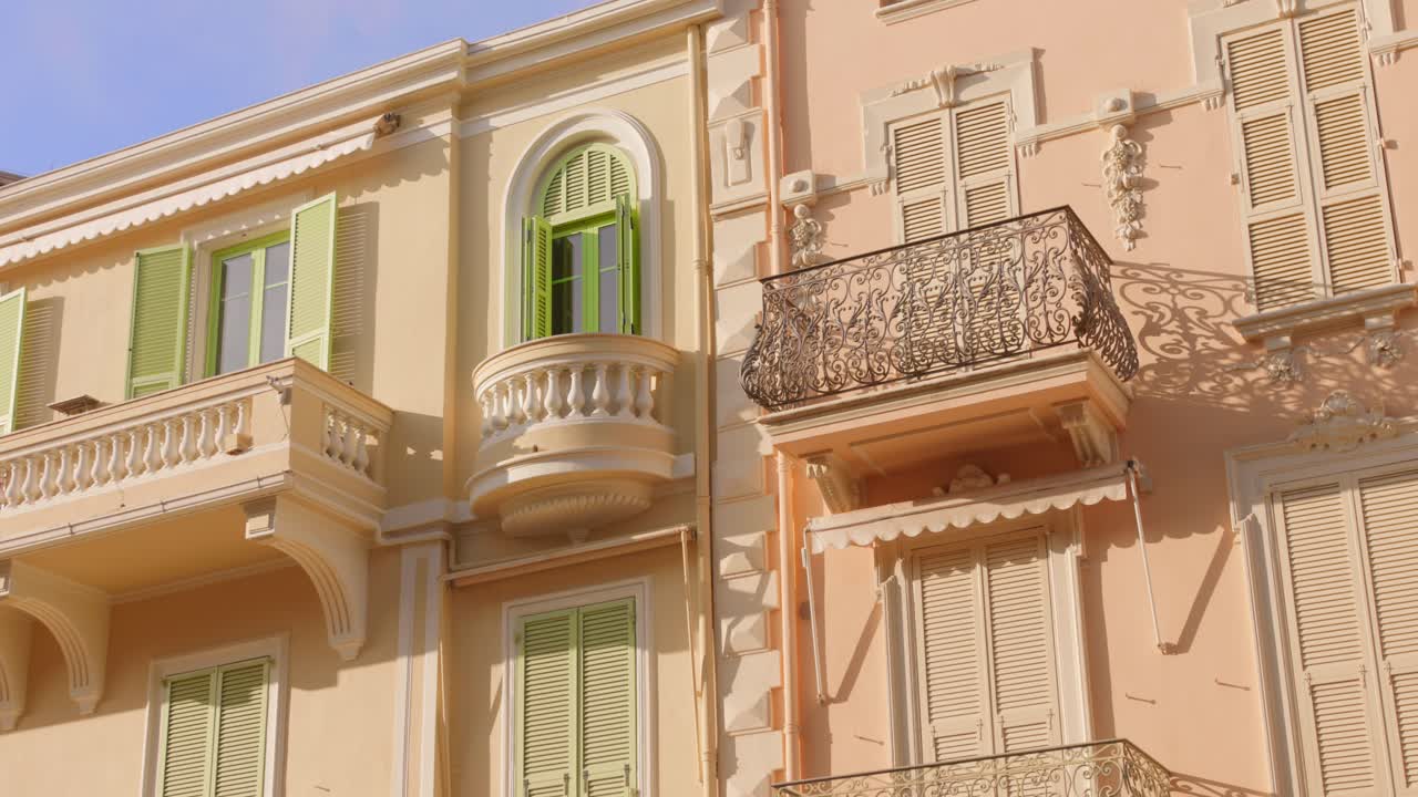 Elegante facciata storica con balconi e persiane verdi nel centro storico di Monaco, illuminata dalla calda luce solare mediterranea.