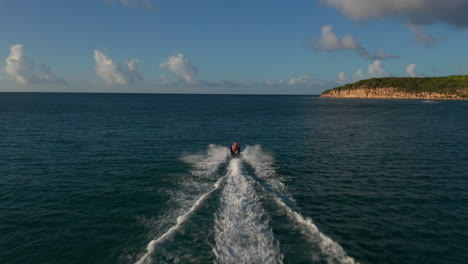 Aerial-top-view-tracking-woman-rides-jet-ski-at-full-speed-on-calm-atlantic-coastline