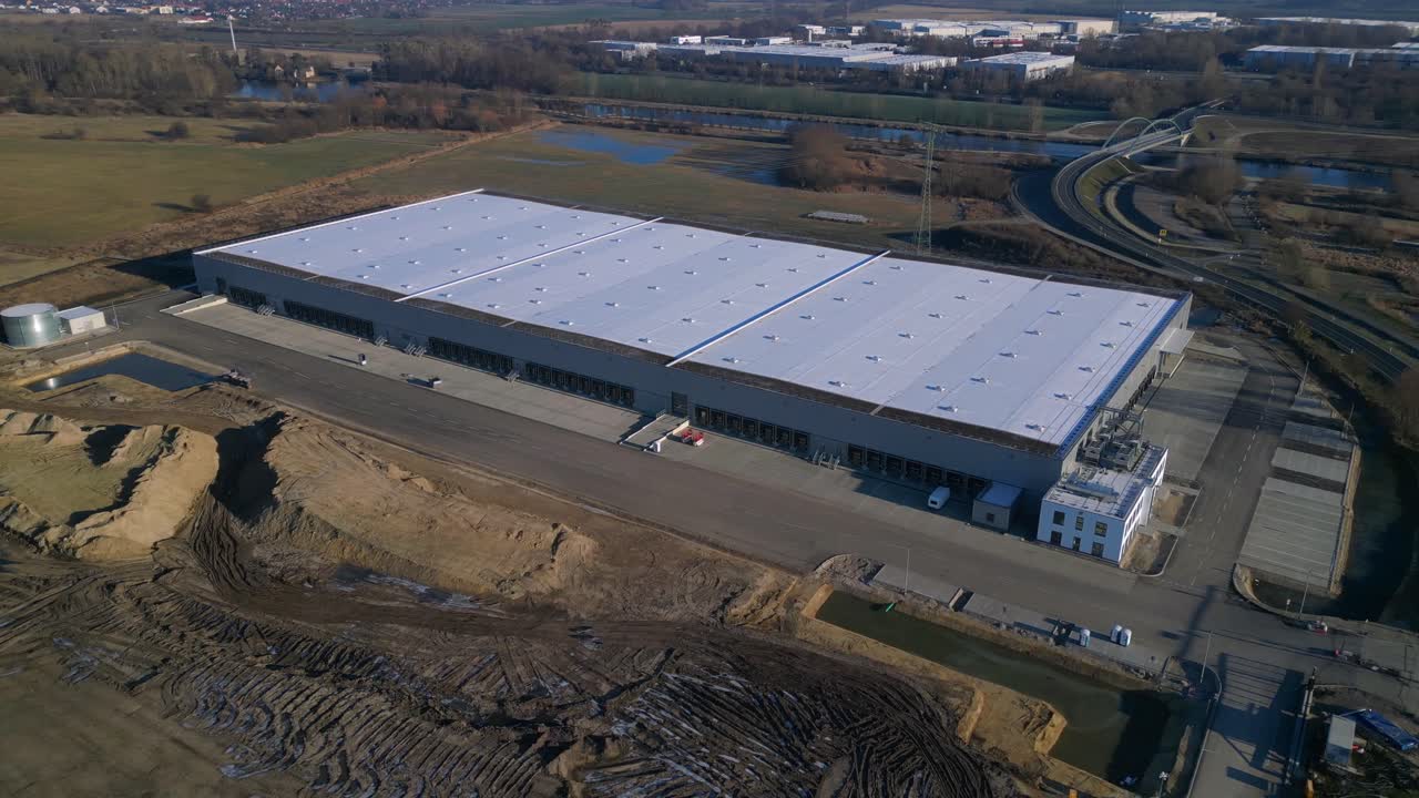 Nuovo grande centro logistico in costruzione con una vasta area di stoccaggio, banchine di carico e terreno vuoto circostante. Incredibile panorama aereo a 360° ripreso con drone