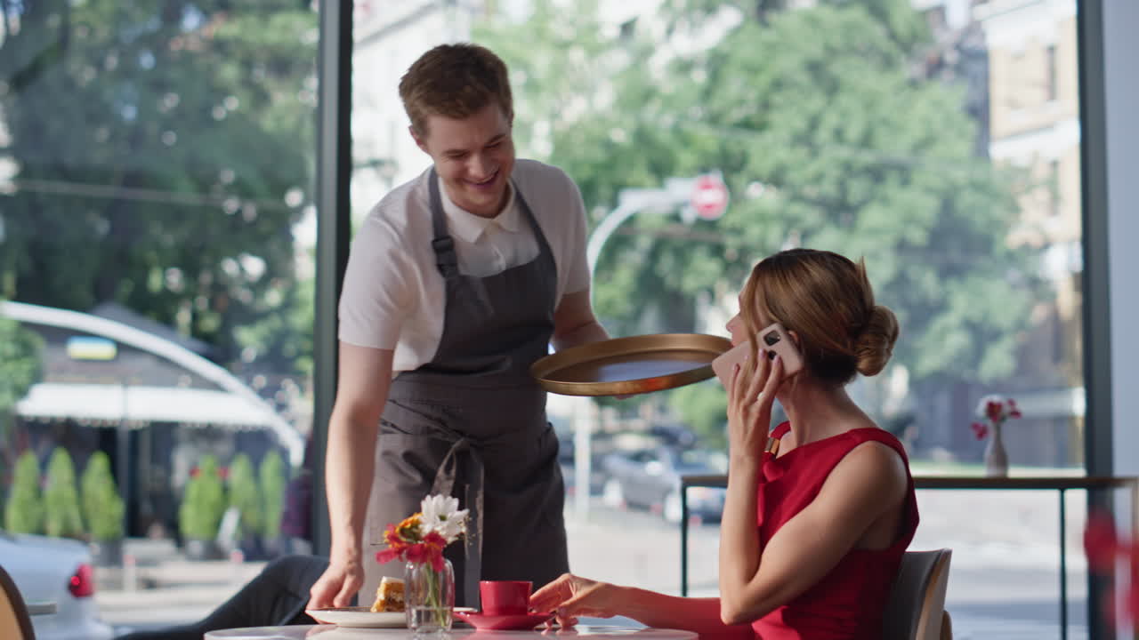Red dress woman calling smartphone in cafe. Waiter bringing lunch to happy lady