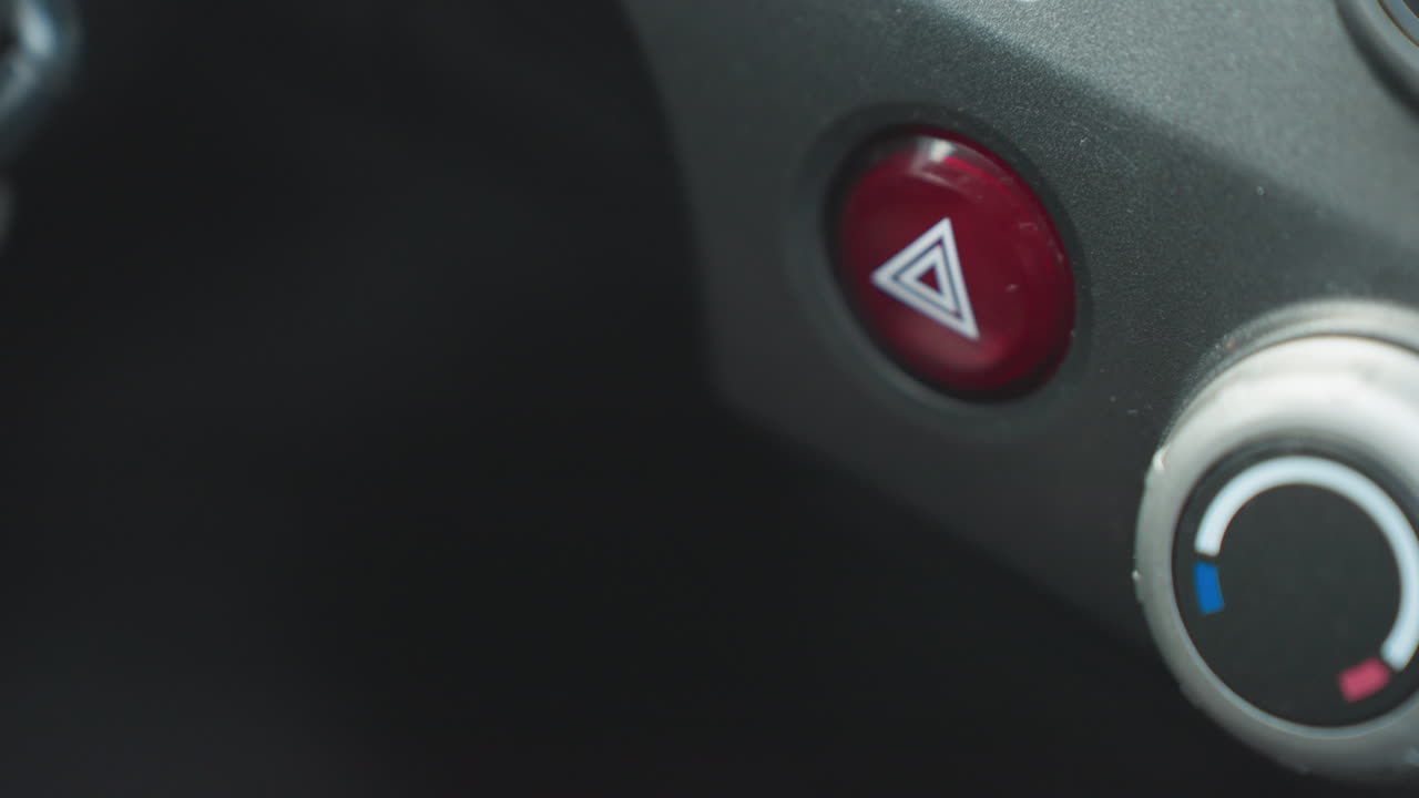 Top down view of individual pressing hazard warning button on car dashboard console showing finger on red triangular emergency icon switch near climate control dial in modern vehicle cabin