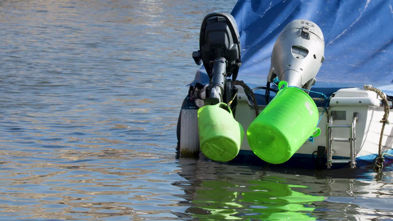 Two small motorboats with green fenders gently bob on calm harbor water in daylight