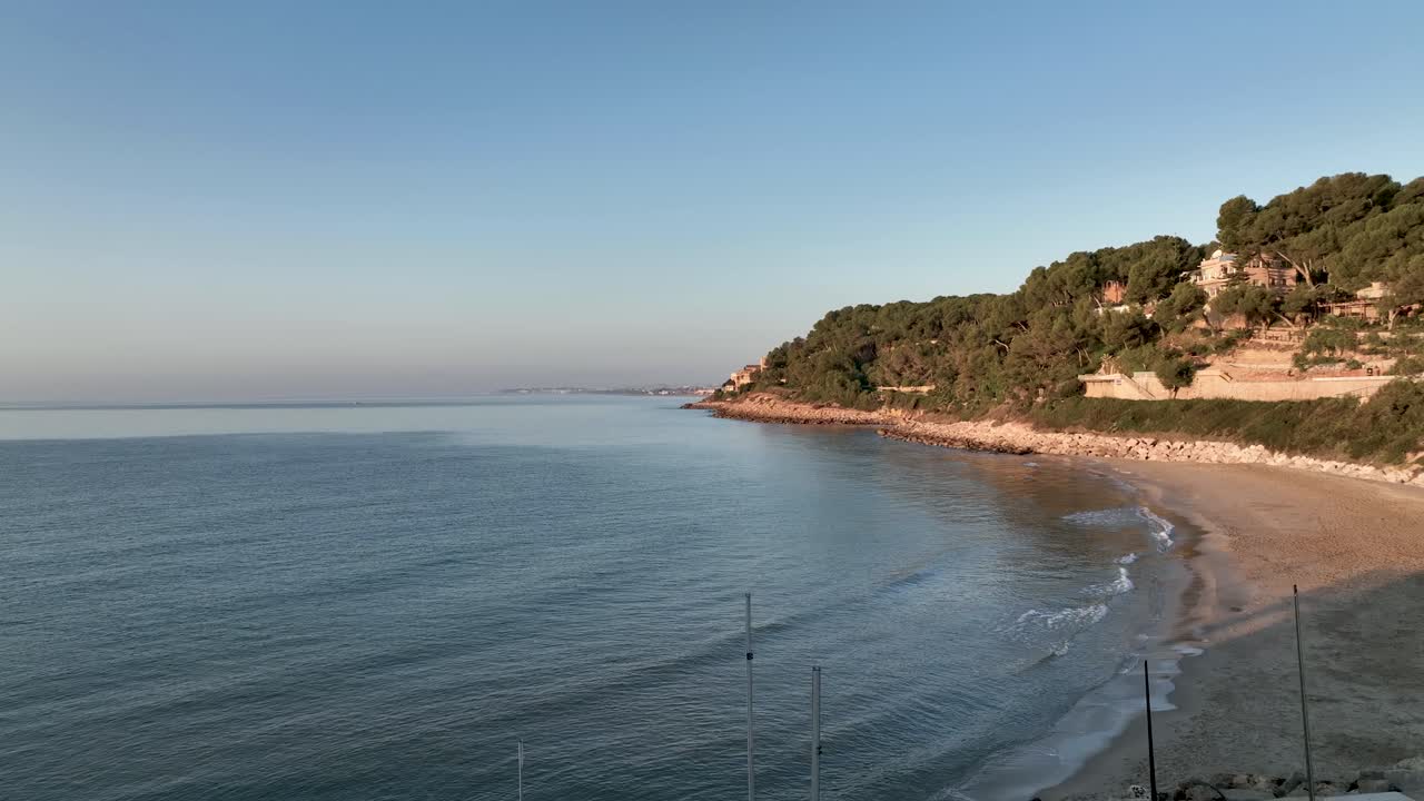 olas tranquilas golpean la orilla de una playa solitaria, donde una suave colina se eleva sobre la superficie del agua