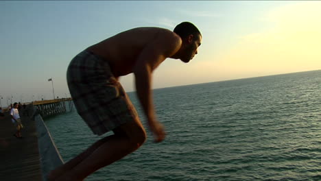 a young man climbs onto the rail of a pier and plunges into the sea