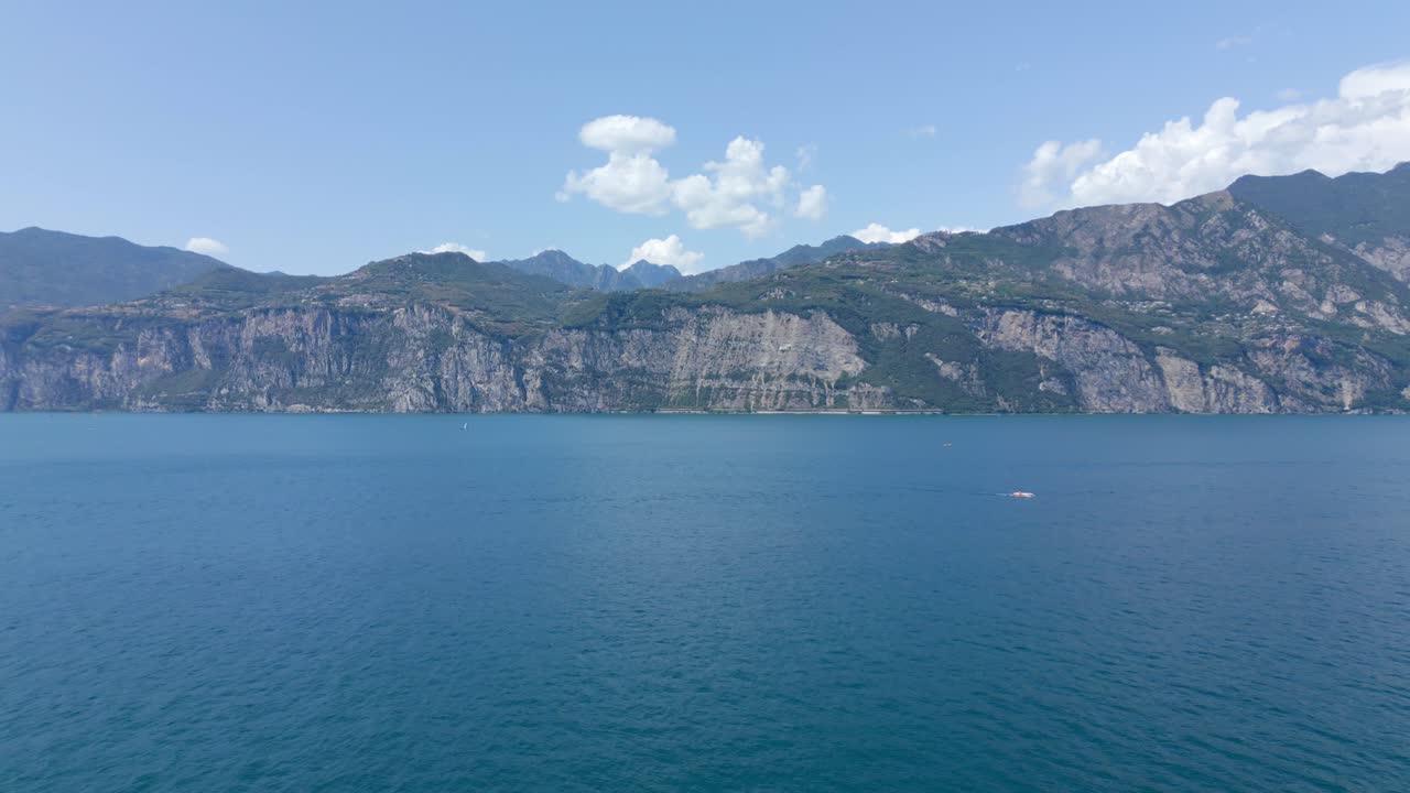 A panoramic aerial shot of the majestic mountains looming over Lake Garda in the charming town of Malcesine, Verona, Italy on a picturesque day with a clear blue sky and fluffy clouds