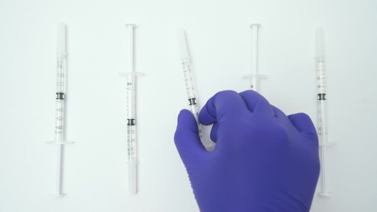 Doctor's hand wearing a protective glove taking one of many medical syringes on a white background