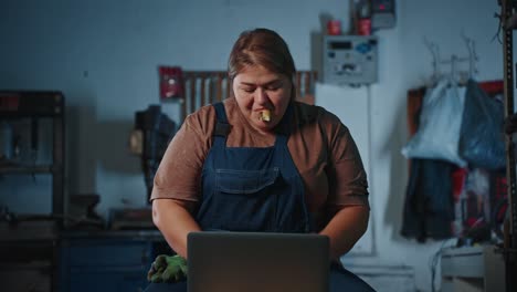 woman mechanic eating while working on laptop in garage