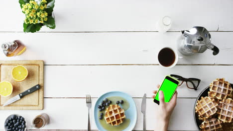 vista superior hombre usando pantalla táctil de teléfono móvil pantalla verde comiendo desayuno gofres belgas y manos de café desde arriba - dragón épico rojo