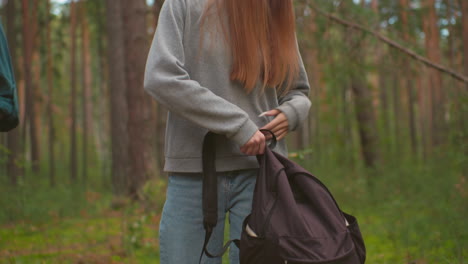 two young hikers walk through a peaceful forest, appearing slightly tired as they carry their backpacks, approaching a fallen tree, the woman in the gray sweater begins to open her black bag