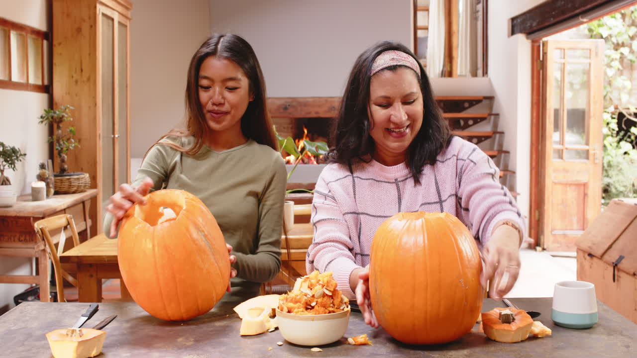 Carving pumpkins together, multiracial young woman and grandmother, at home, Halloween time