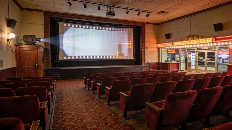 Projector casting beam onto glowing screen in empty cinema with red seats, AI-generated