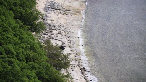 Close-up-of-a-rocky-beach-with-calm-waves-rolling-in,-high-angle-landscape,-4K