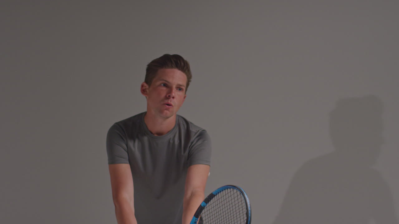 남자 테니스 선수가 회색 배경에 라켓으로 공을 때리는 경기장에서 촬영된 스튜디오  3