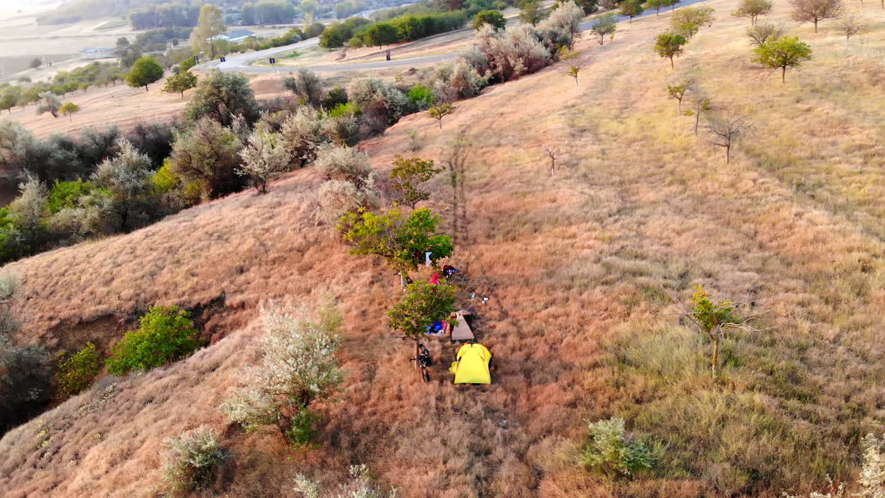 Aerial drone view of camping tents with people in the meadow. Beautiful sunset in Moldova. Greenery and village on background. Travel time idea