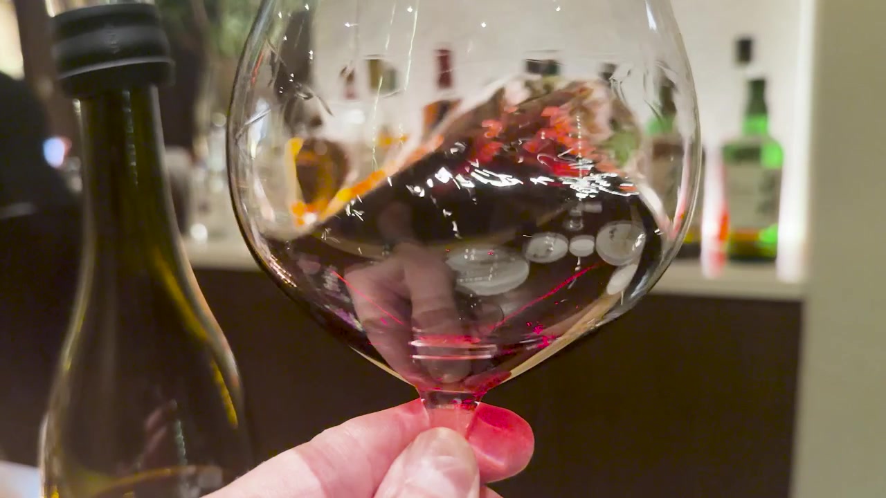 A close-up shot of red wine swirling in a glass at a dimly lit bar