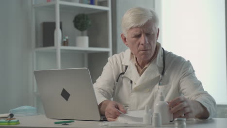 a grey haired, middle aged doctor consults on a notebook the composition of a medicine