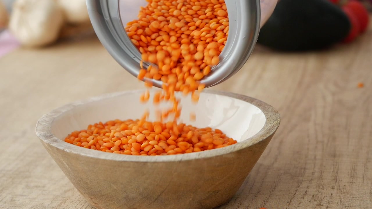 Lentilles corail versées d'un récipient dans un bol en bois