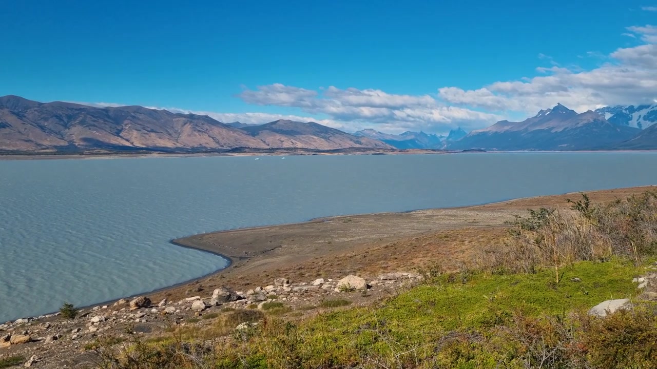Panoramaudsigt over Lago Argentino på en solskinsdag, der viser det enorme patagonske landskab med de tårnhøje Andesbjerge i baggrunden