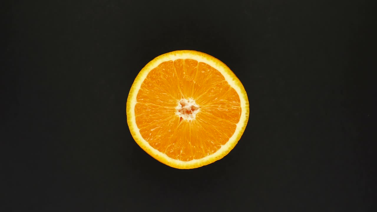 Arancia rotante su sfondo nero. Succhi freschi, frutta, vitamine e concetto estivo. Vista dall'alto di mezzo agrume succoso