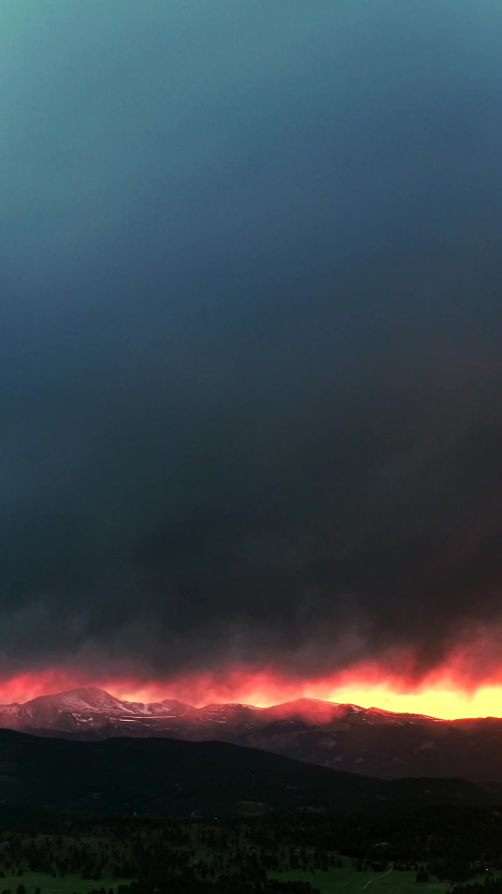 Sonnenuntergang, goldene Stunde, leuchtend orangefarbener, feuriger Himmel, dunkle Gewitterregenwolke, Frühlingsschnee bedeckter Mount Blue Sky, Luftaufnahme Drohne, Colorado, vertikale Rocky Mountains, Mount Evans Wilderness, Gipfel der Front Range, Panorama.