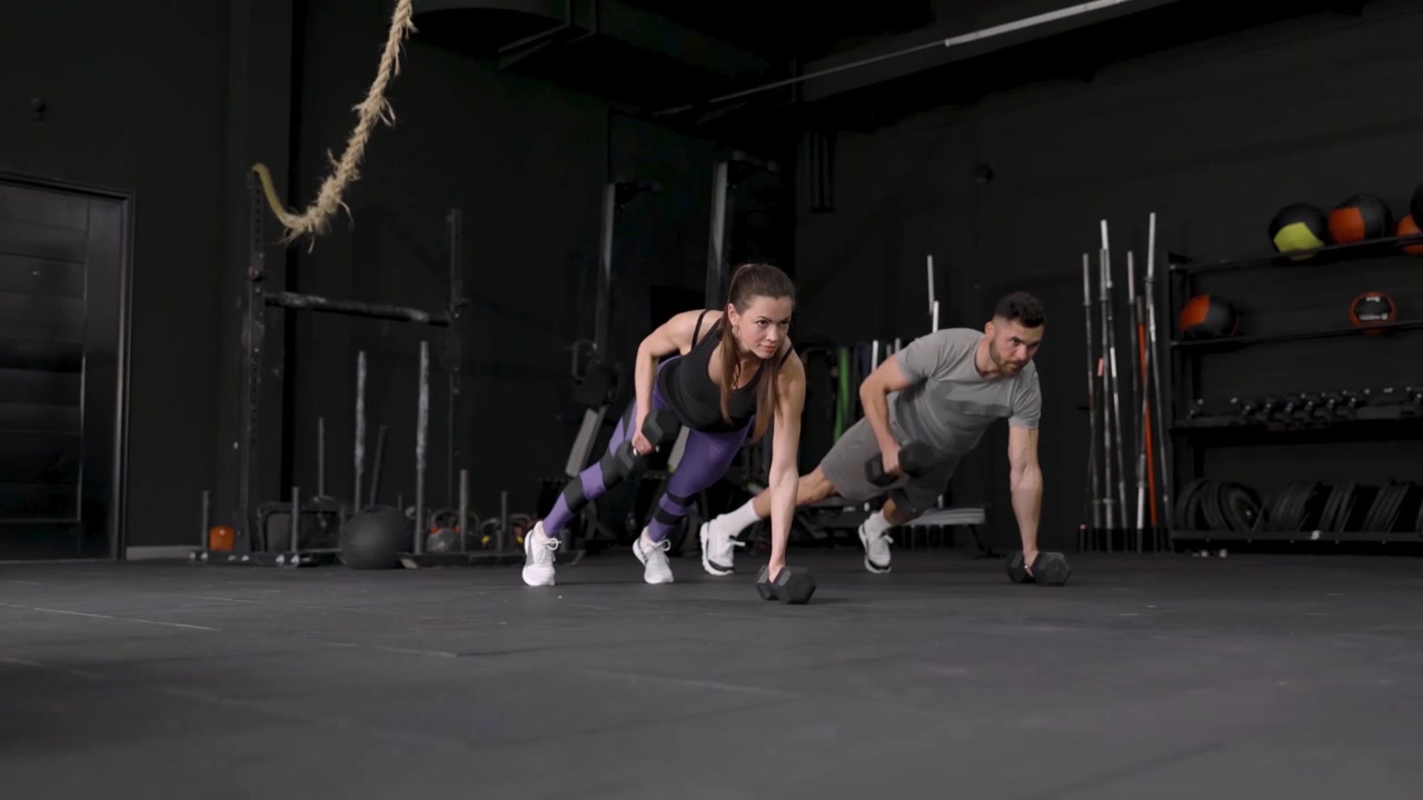 Hombre y mujer en forma haciendo ejercicio con mancuernas en posición de plancha