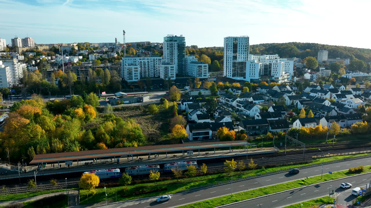 Drone shot of a residential neighborhood with tall apartment buildings, autumn trees and a busy railway station with a passing train - Gdynia
