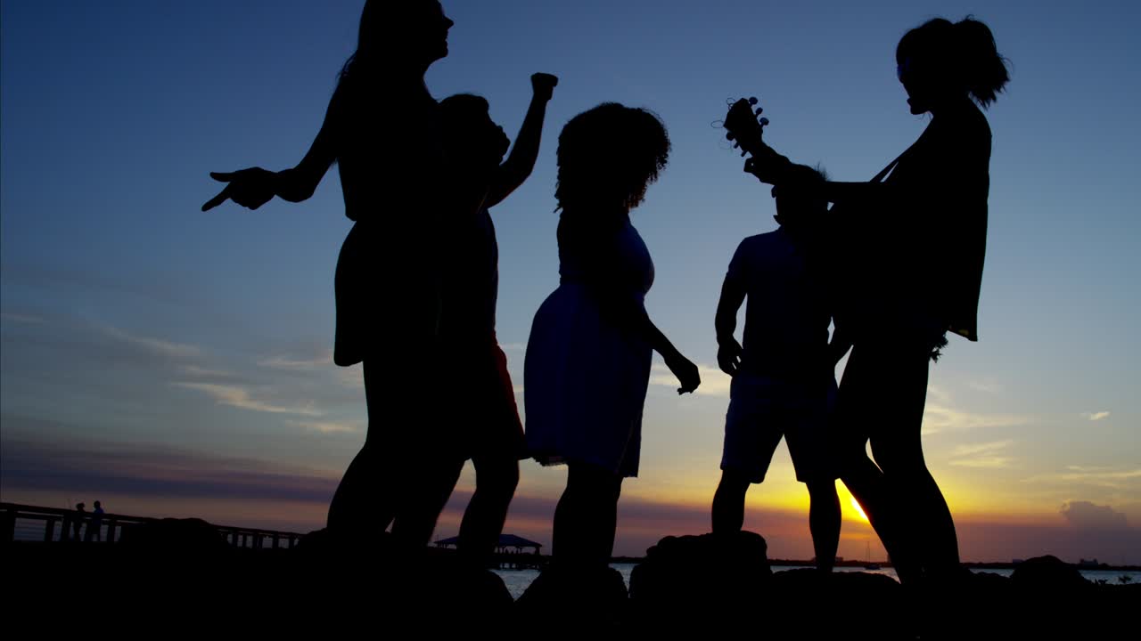 해가 지는 해변에서 춤을 추는 사람들의 실루