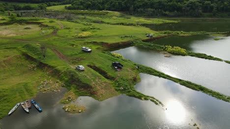 aerial footage over the water towards the edge of the forest revealing boats, vehicles people, fishing and enjoying nature, muak klek, saraburi, thailand