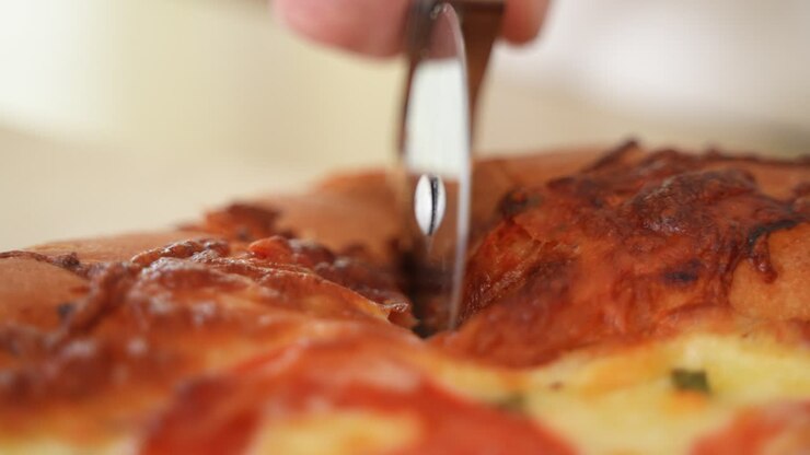Taglio di pizza Margherita croccante con rotella tagliapizza, verso la telecamera, carrellata all'indietro