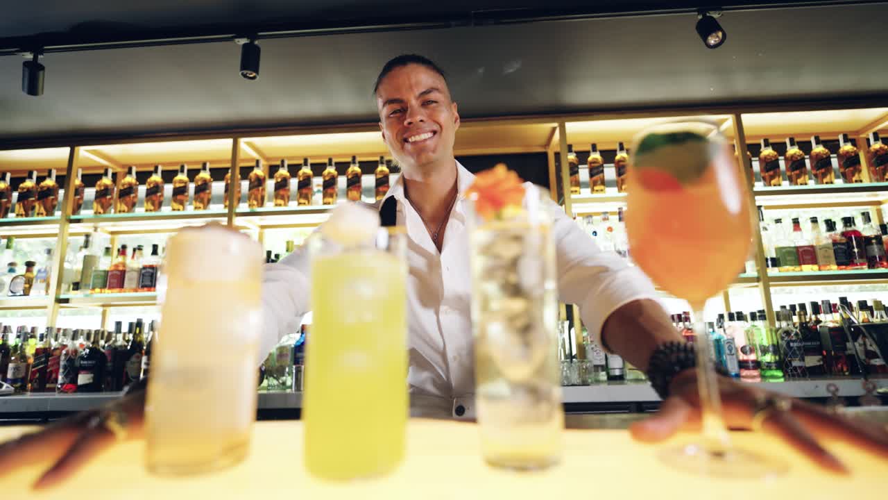 Barman sorridente che presenta quattro cocktail colorati in un bar moderno