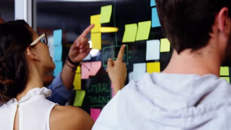 Male-executive-writing-on-sticky-notes-while-colleagues-discussing-during-meeting