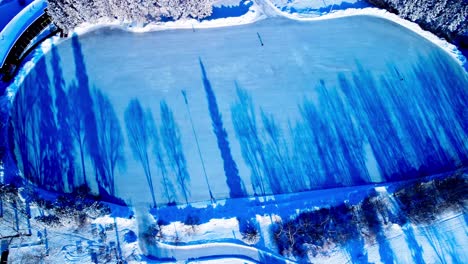 icy cold winter aerial birds view flyover canada's largest outdoor skating rink spanning the size of 8 nhl hockey arenas sunset reflection of trees shadow on ice with less than a handful of skaters