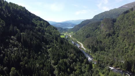 Looking-towards-Lonavatnet-and-Voss-center-from-Strandaelvi-river-and-Vinje-with-road-E16-on-the-side---Beautiful-summer-day-aerial-from-lush-valley-in-Voss-area-Norway