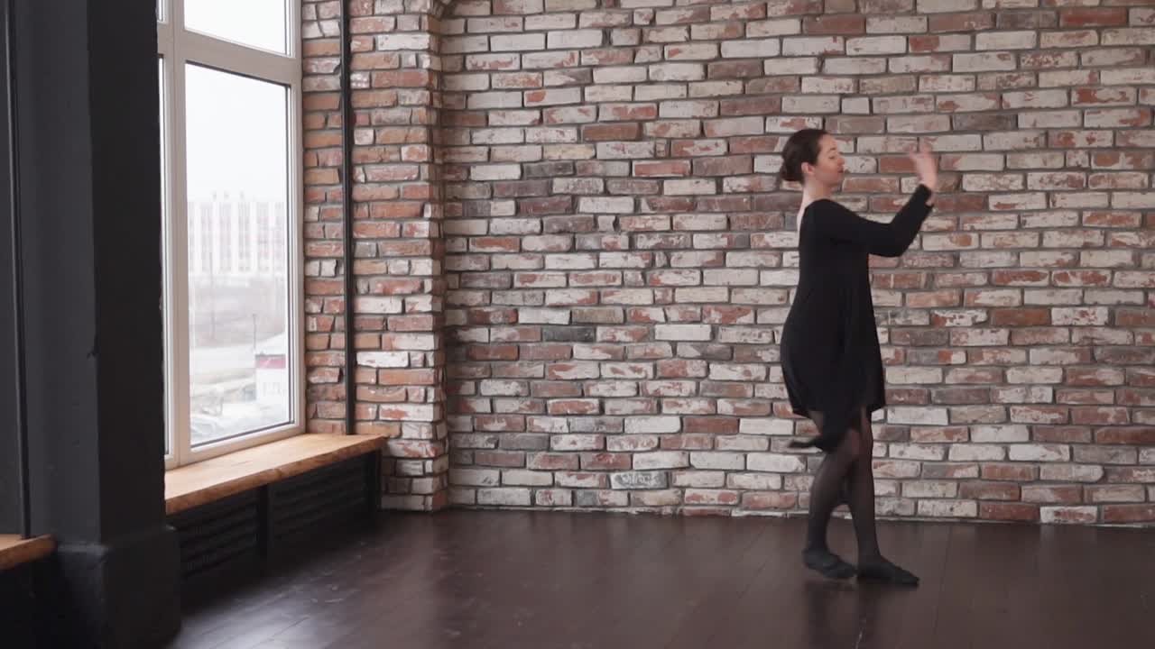 검은 드레스 를 입은 발레 댄서 가 벽돌 스튜디오 에서 공연 하고 있다