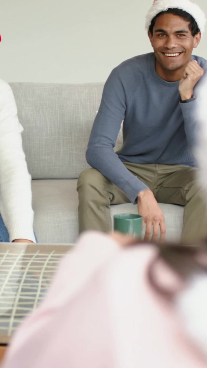 Vertikal video: Ser en hånd række ud, mænd med nissehuer læner sig på sofaen, åbner håndfladerne mod barn, krus