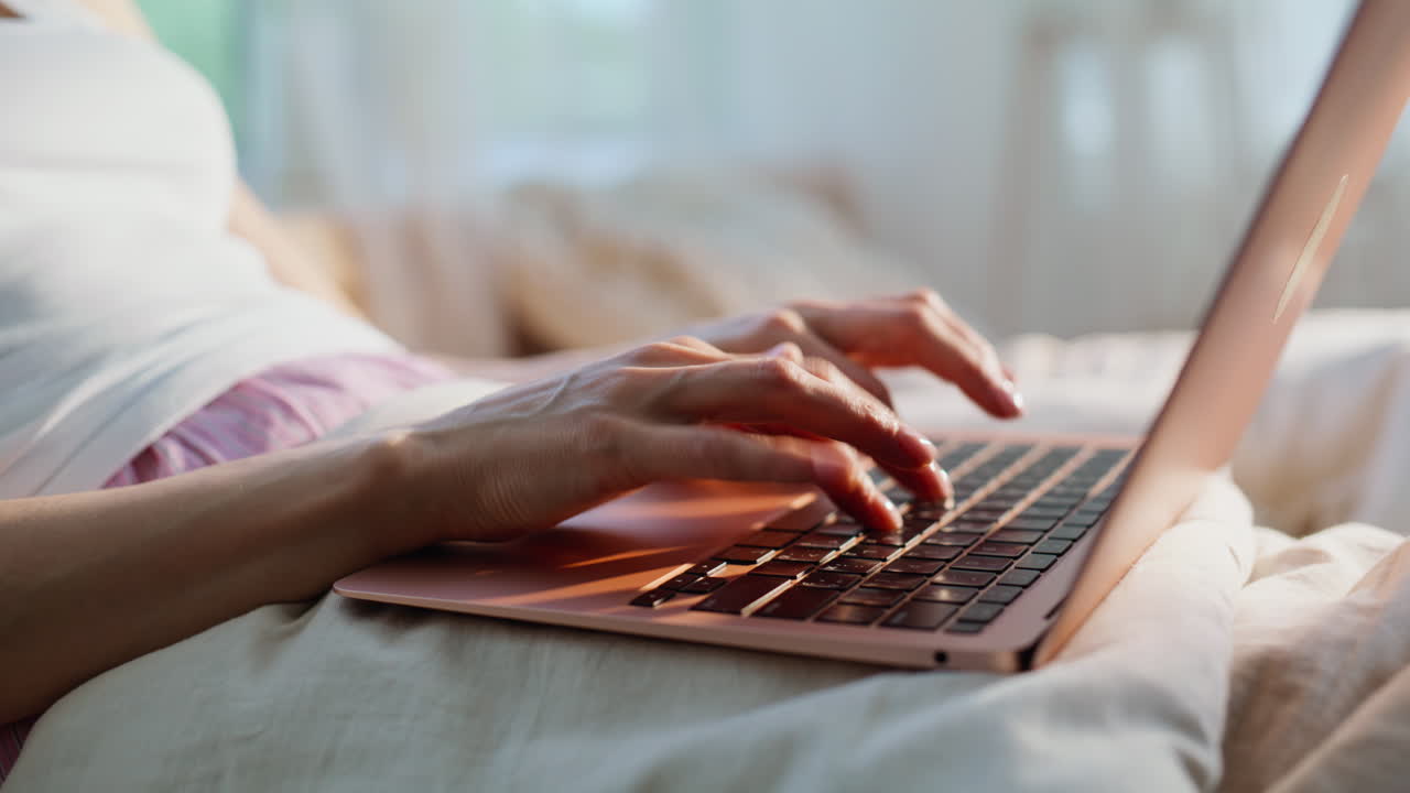 Close-up de mãos de estudante digitando em um teclado sobre a roupa de cama em um apartamento. Freelancer mulher