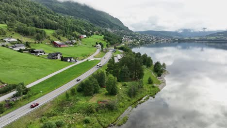 autobús y coches en la carretera e16 a voss noruega - aérea siguiendo el tráfico desde el lado antes de ascender por encima de la carretera para revelar una vista panorámica de voss y el cristalino lago vangsvatnet