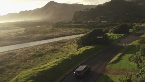 suv driving along a thin road during the golden hour at north piha beach in auckland, new zealand as a misty lit horizon lies ahead